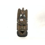 A DARK WOOD HAND-CARVED TRIBAL MASK WITH DECORATIVE INLAY DESIGNED TO REFLECT THE INITIATION OF