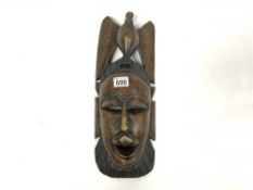 A DARK WOOD HAND-CARVED TRIBAL MASK WITH DECORATIVE INLAY DESIGNED TO REFLECT THE INITIATION OF