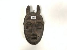 CIRCA 1920 RED HARDWOOD CARVED MASK WITH SHORT HORNS, SCAR MARKS TO THE CHEEKS AND SQUARE MOUTH WITH