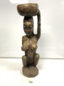 A CARVED WOODEN SEATED TRIBESMAN WITH A BOWL ON HER HEAD