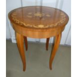 A circular musical side table, the hinged top inlaid with flowers and a leaf border on four cabriole