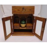 An oak rectangular smoking cabinet with glazed hinged doors revealing a pipe rack and a ceramic