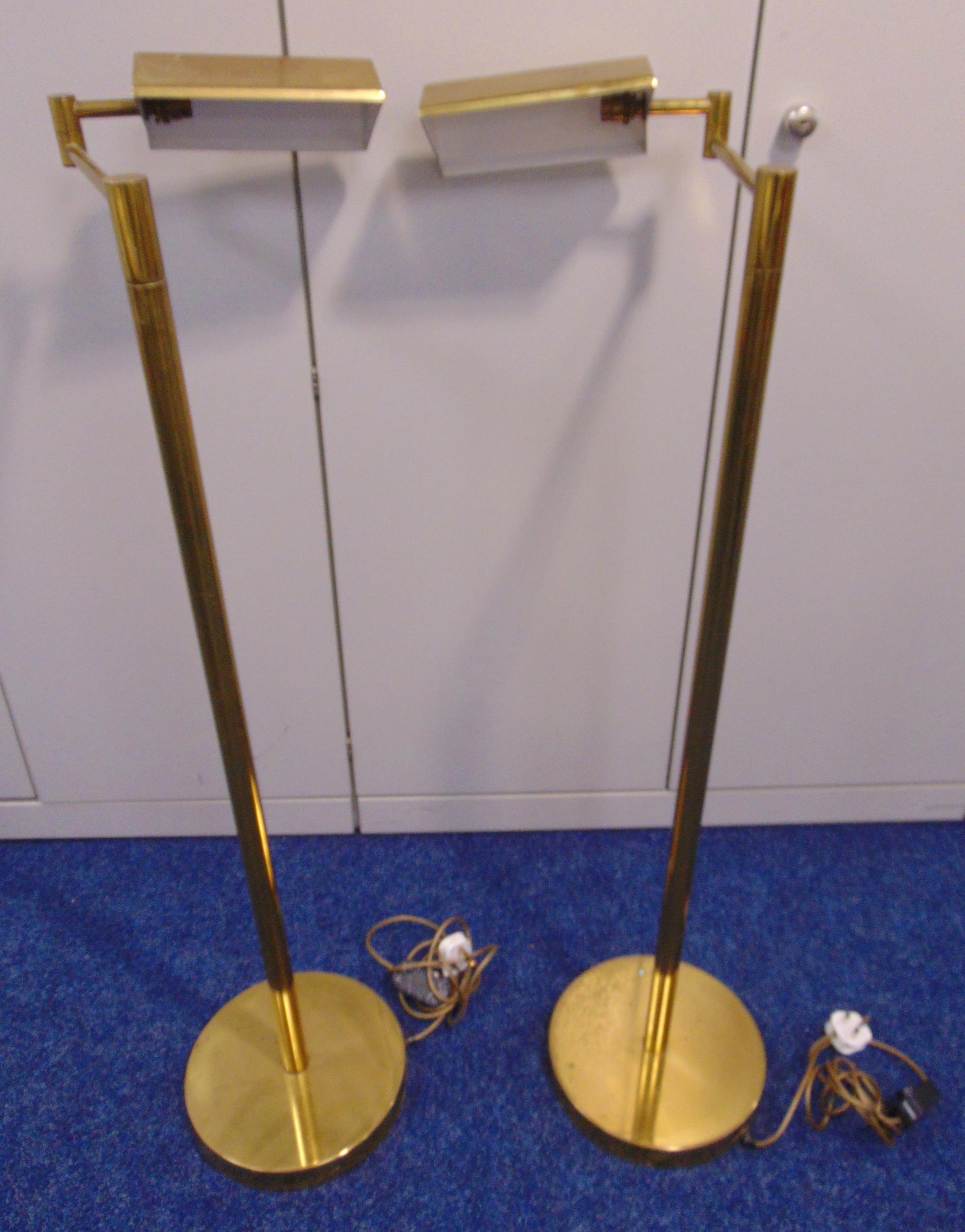 A pair of brass standard lamps, tubular with angled rectangular shades on raised circular bases,