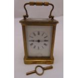 A brass carriage clock of customary form, white enamel dial with Roman numerals to include a key,