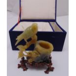 A carved hard stone figurine of a bird sitting on a branch with hardwood stand in original case,