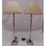 A pair of silver plated table lamps of elongated columnular form on raised stepped square bases with