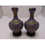 A pair of cloisonné baluster vases decorated with stylised leaves and scrolls on carved hardwood