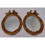 A pair of oval gilded frame wall mirrors surmounted by Putti figurines, 33 x 25cm
