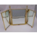 A gilded metal three panel dressing table mirror with urn finials on spool feet, 56 x 86cm