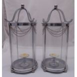 A pair of chrome and glass storm lanterns, cylindrical with suspensory chains on four ball feet,