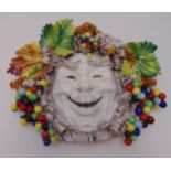 An Italian ceramic Majolica wall plaque in the form of a masked jester with leaf and berry surround,