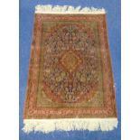 A Persian silk and wool carpet with central medallion and floral surround, red against a blue