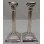 A pair of hallmarked silver Corinthian column table candlesticks on raised stepped square bases with