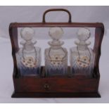 A three bottle oak Tantalus with three cut glass decanters and enamel wine labels, 33.5 x 35 x 13cm