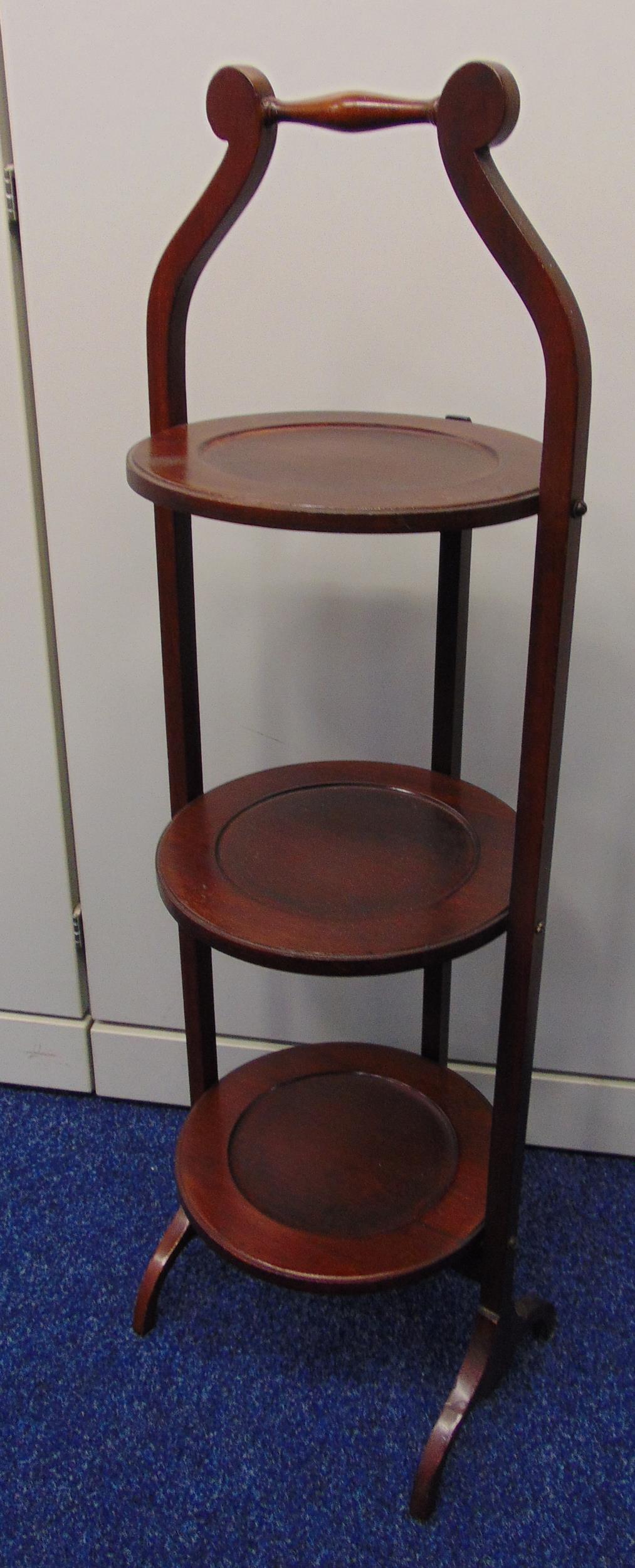 A mahogany three tier plate stand of customary form on scroll supports, 87.5cm (h)