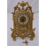 A gilded metal easel clock with scroll pierced frame surmounted by an urn on four square feet, the