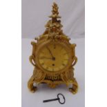 A gilded metal mantle clock, the engine turned circular dial with Roman numerals within a Rococo