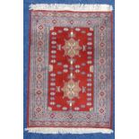 A Middle Eastern red ground carpet with two central medallions within a geometric border, 113 x 80.