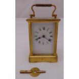 A brass carriage clock of customary form, white dial with Roman numerals and swing handle, to