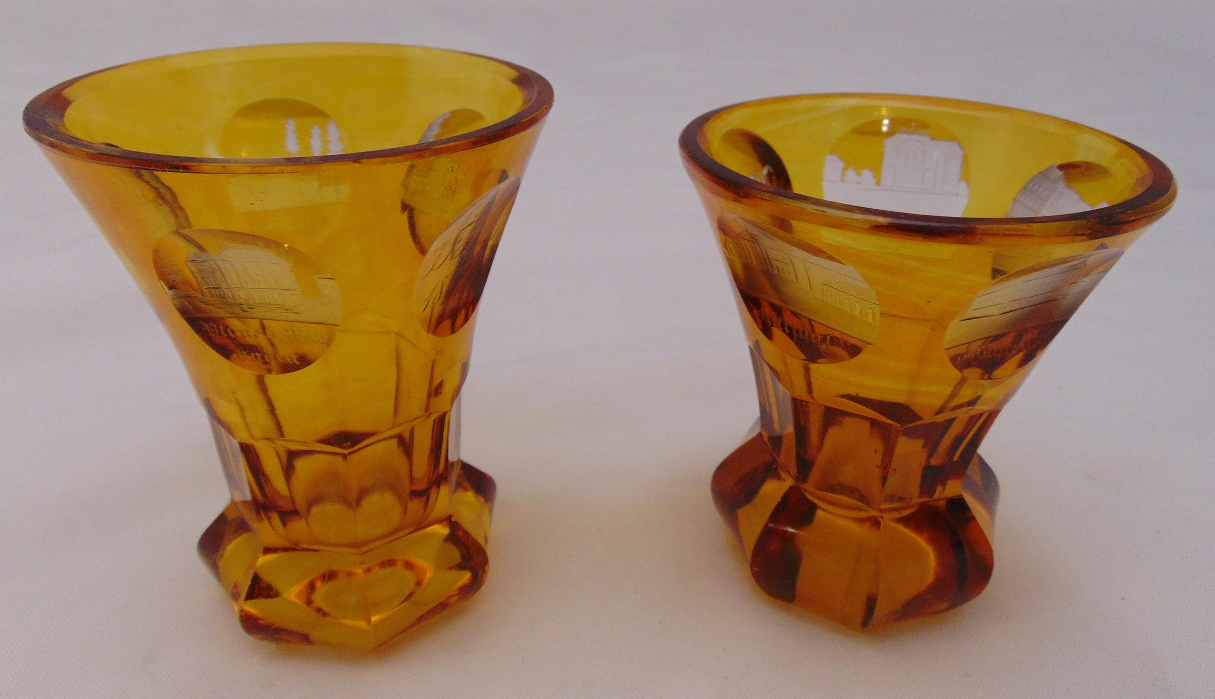 Two Bohemian amber glass beakers etched with roundels of historic buildings one dated 1838, 11cm and