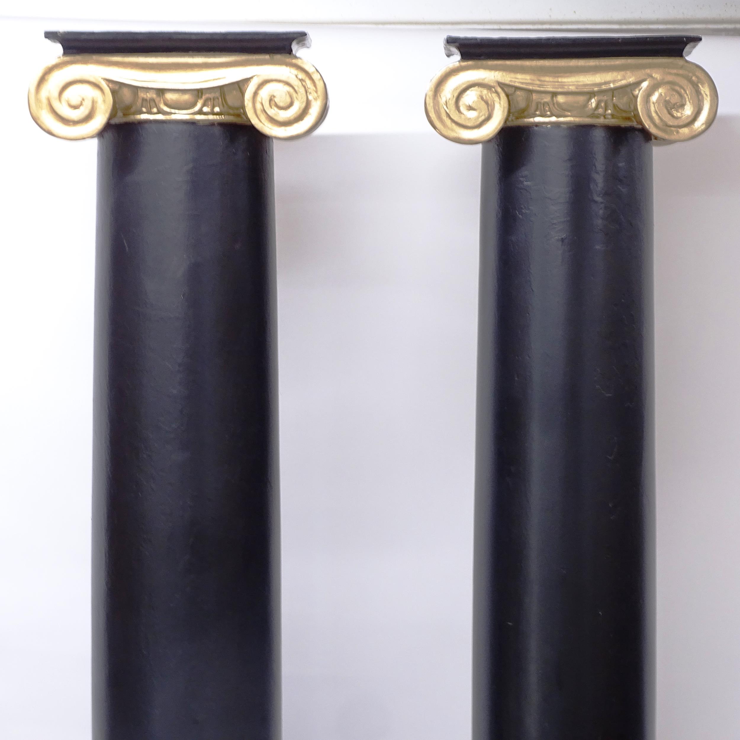 A pair of fibreglass Ionic columns painted in black and gold, H229cm