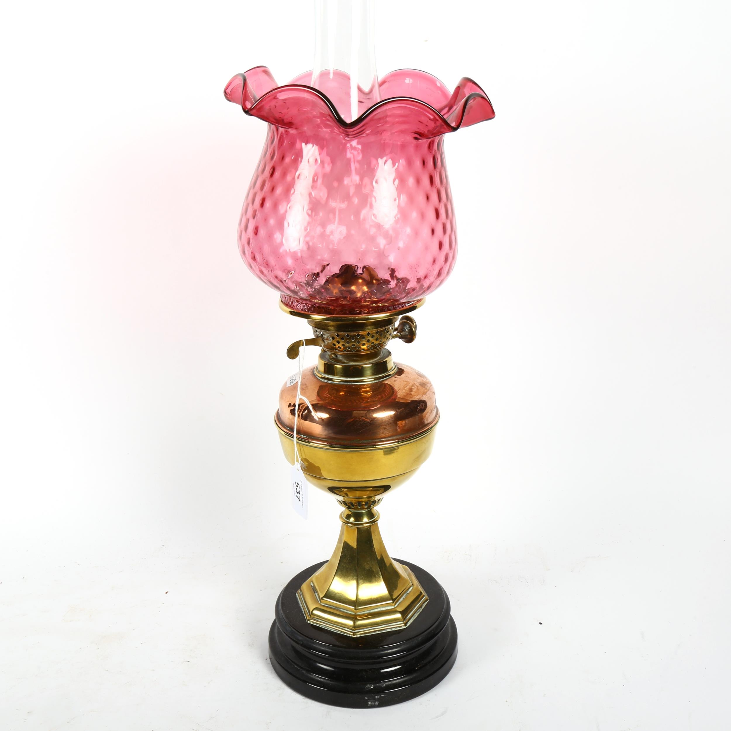 A Victorian brass and copper oil lamp on plinth, with chimney and cranberry glass shade, 59cm