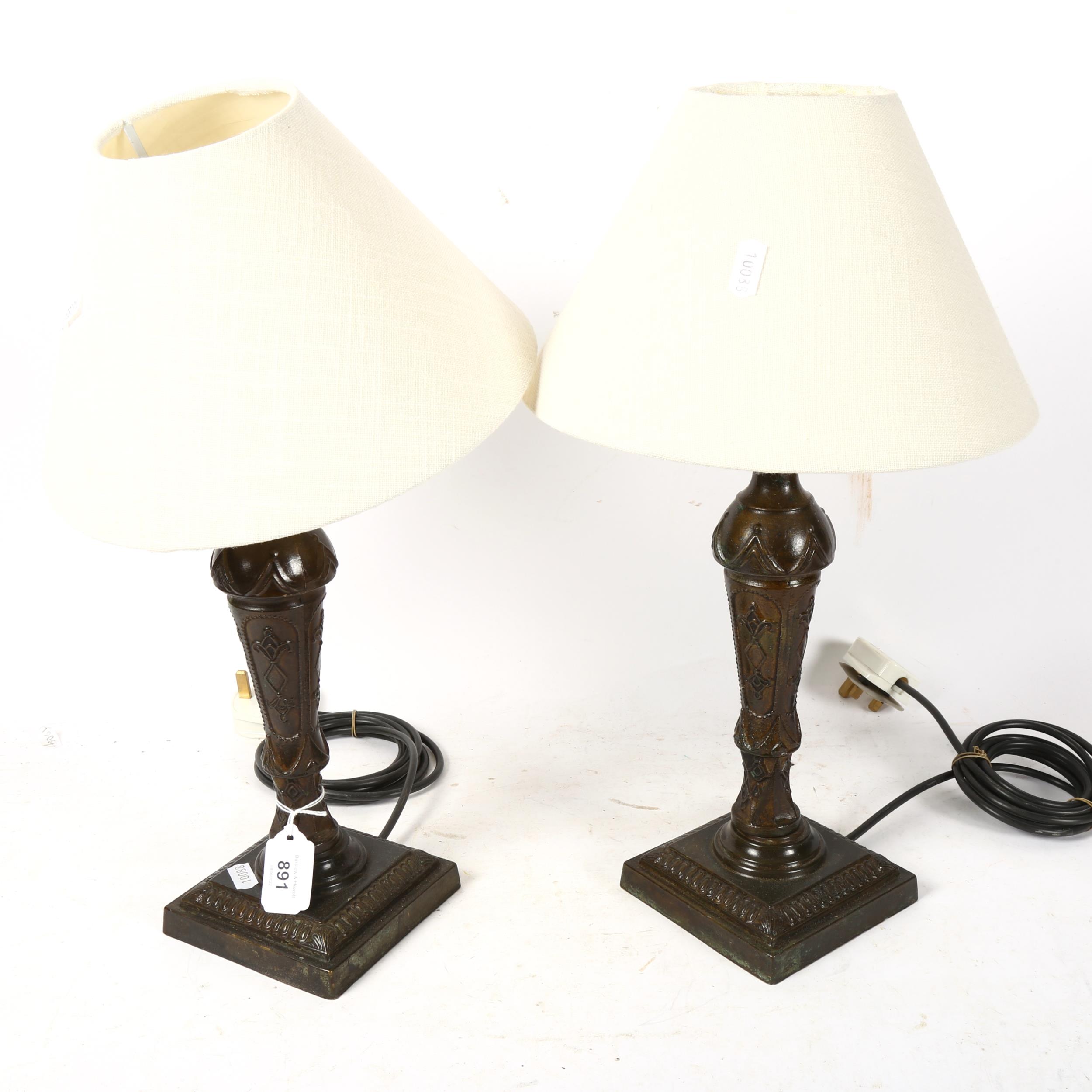A pair of patinated cast-brass table lamps, in Classical design, with cream shades, height 44cm