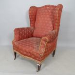 An early 20th century mahogany and upholstered wingback fireside armchair (for reupholstery)