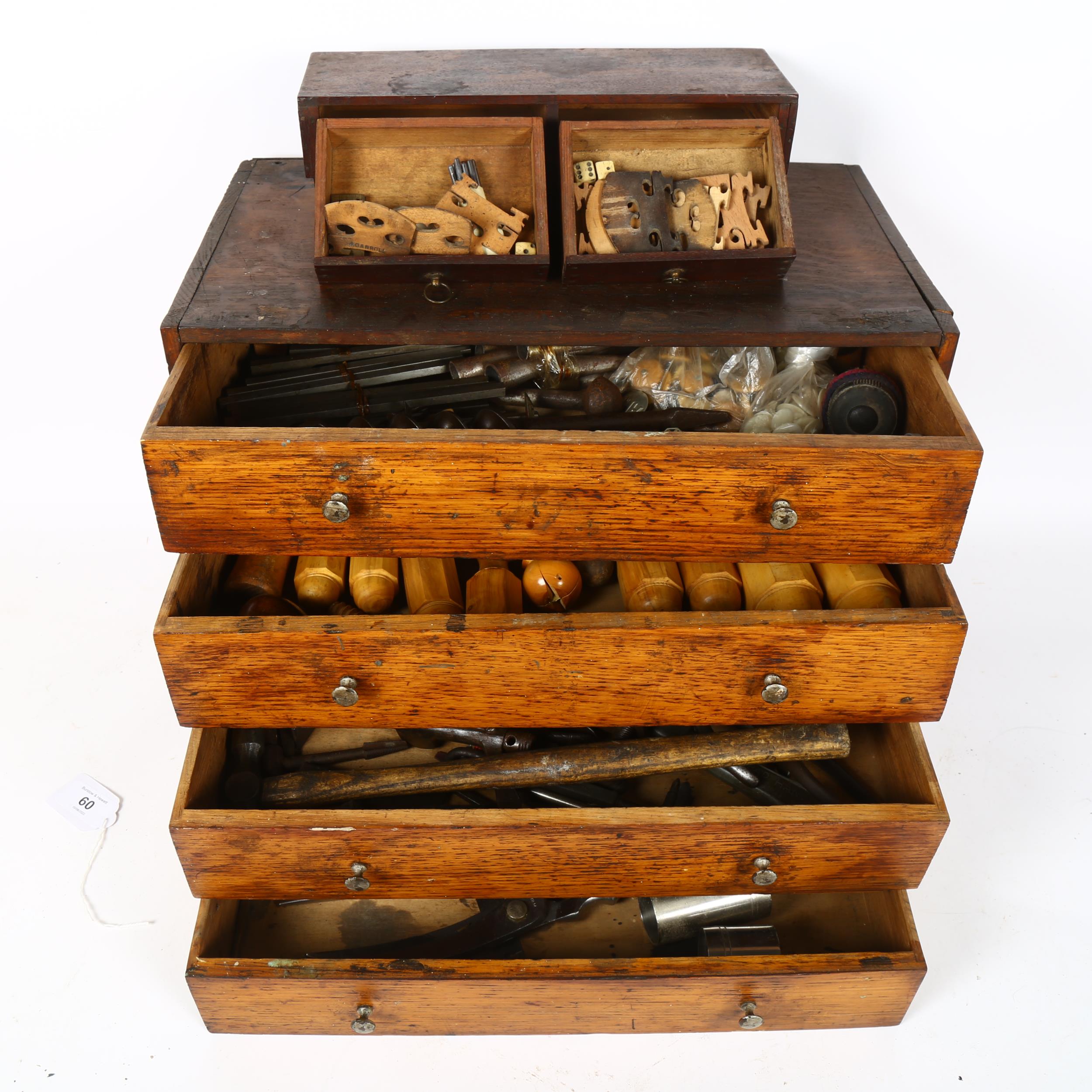 A stained oak carpenter's table-top chest of drawers, filled with various tools, drill bits,