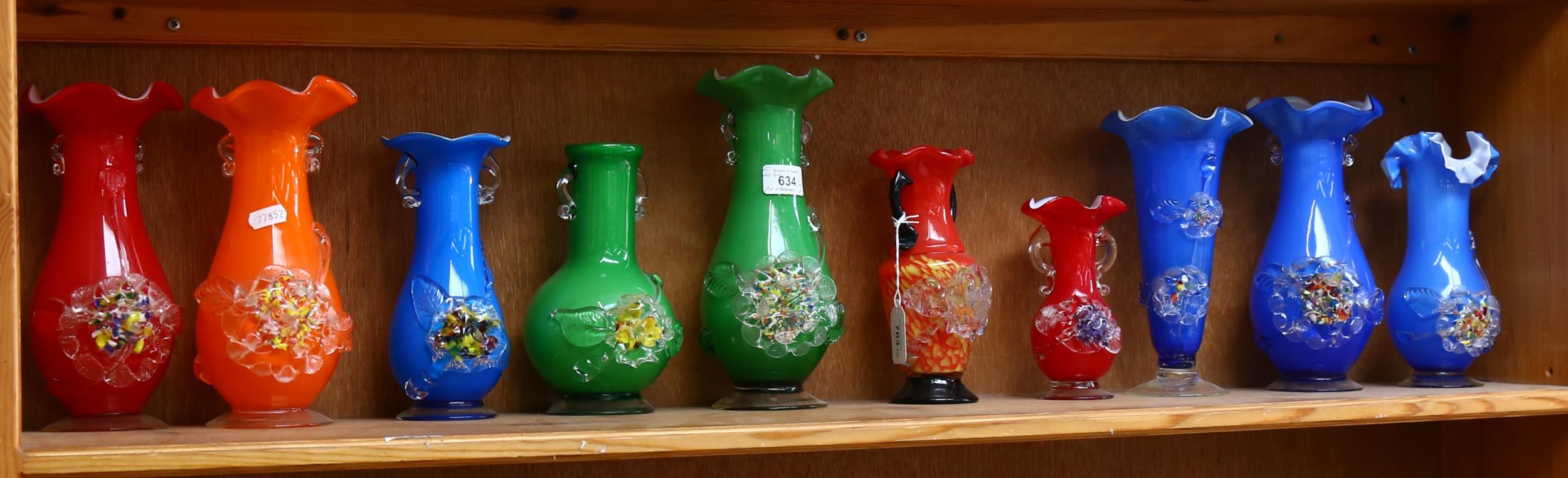 A shelf of colourful 1950s glass vases with applied floral decoration, tallest 25cm