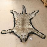 TAXIDERMY - an early 20th century leopard skin rug, with head bearing teeth, on felt backing, length