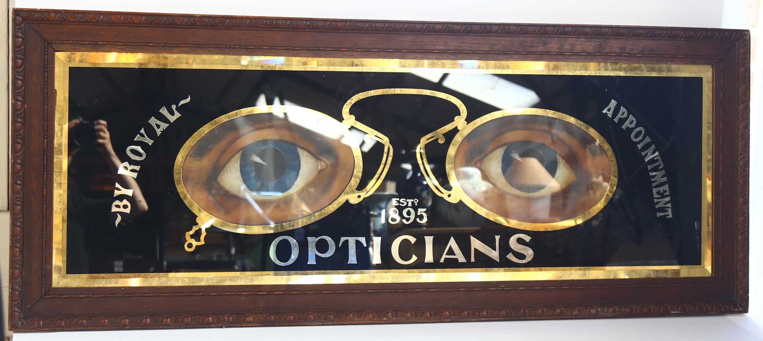 A large Optician's advertising sign, in carved mahogany framed, overall 54cm x 135cm