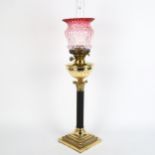 An early 20th century brass duplex Corinthian column oil lamp, with cranberry glass shade and