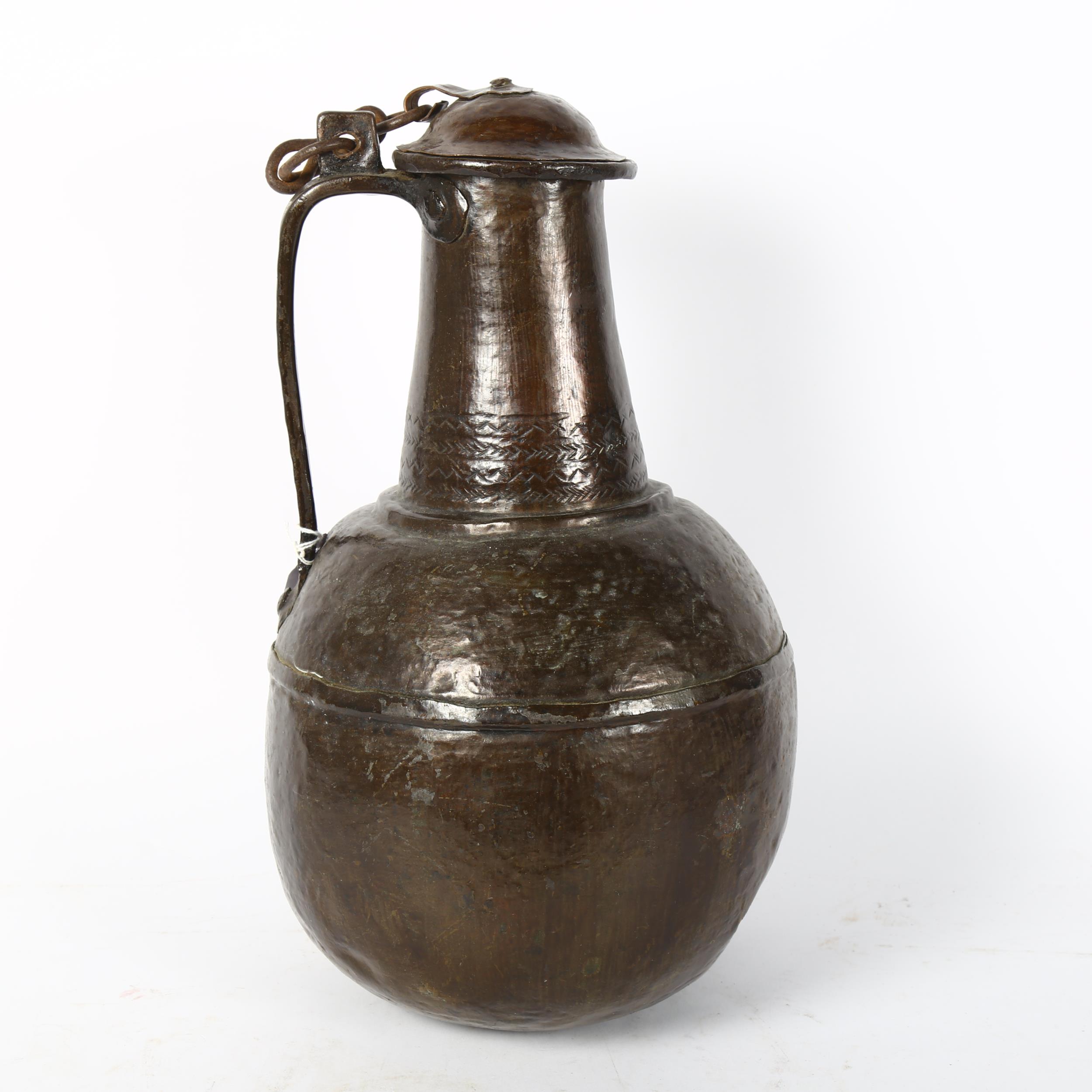 A Middle Eastern handmade copper wine flagon and cover, engraved geometric decoration to the lid,