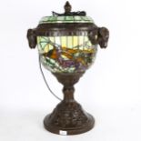 A Tiffany style urn design lamp on cast-metal support, with ram's head handles, and multi-coloured