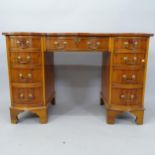 A reproduction yew wood serpentine-front kneehole writing desk, with tooled and embossed leather