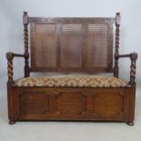 A 1920s oak hall settle with cane-panelled back, lifting seat and carved decoration, 106 x 108 x