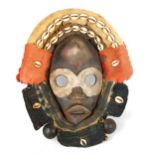 An African Dan carved and painted wood mask, with cowrie shell and textile surround, length 32cm