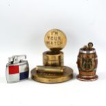 A brass match-striker stand, an Omega blue and red pocket lighter, and a souvenir barrel design