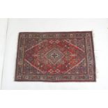 Persian woollen rug, centred with a pole medallion against a red ground with blue flowerhead