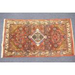 Pakistani small red ground woollen rug, centred with a blue and fawn lozenge medallion, 147cm x 80cm