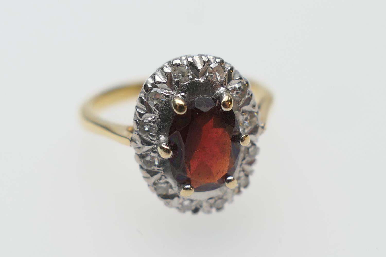 Diamond and garnet cluster ring, the oval garnet of approx. 7mm x 5mm bordered with small round