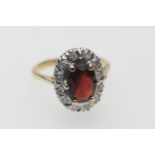 Diamond and garnet cluster ring, the oval garnet of approx. 7mm x 5mm bordered with small round