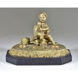 A Gilt Metal Inkwell, Late 19th Century, cast with a child and dog, on polished slate base, 6ins