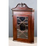 A George III Mahogany Hanging Corner Cupboard, with moulded scroll pediment with urn pattern finial,