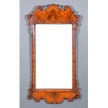 A George III Figured Walnut Wall Mirror, the moulded frame with shaped cresting and apron, inset