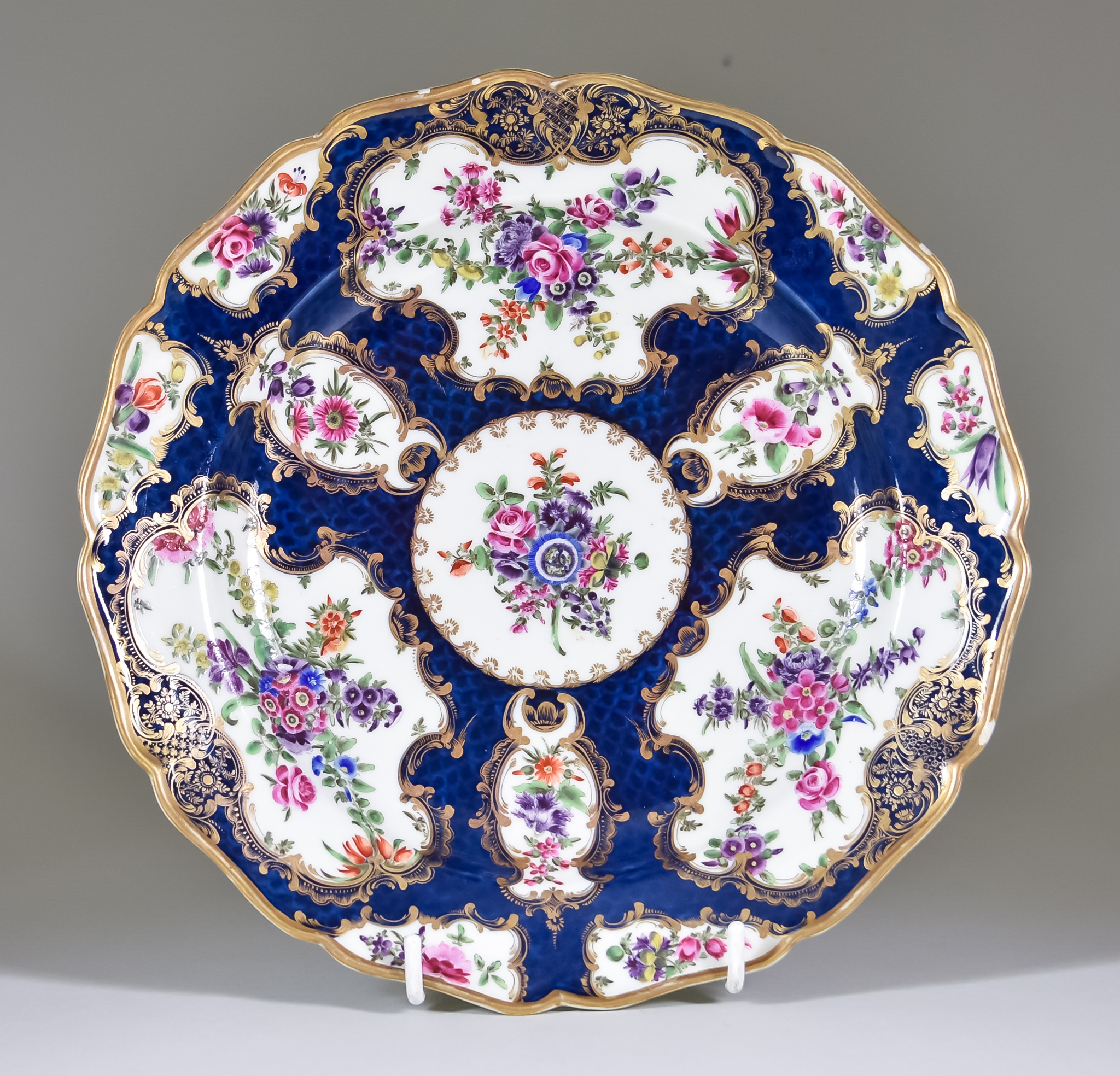 A Worcester Plate, Circa 1765, of shaped outline, enamelled in colours with a blue scale ground,