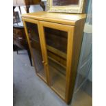 A WOOD EFFECT SMALL BOOKCASE, ENCLOSED BY TWO GLAZED DOORS