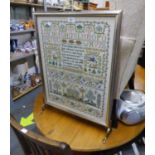 A BRASS CHEVAL GRATESCREEN WITH GLAZED AND NEEDLEWORK SAMPLER PANEL WORKED BY JOYCE KENNEDY