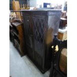 AN OAK TWO DOOR BOOKCASE WITH LEADED GLASS PANELS OVER LINEN FOLD DECORATION